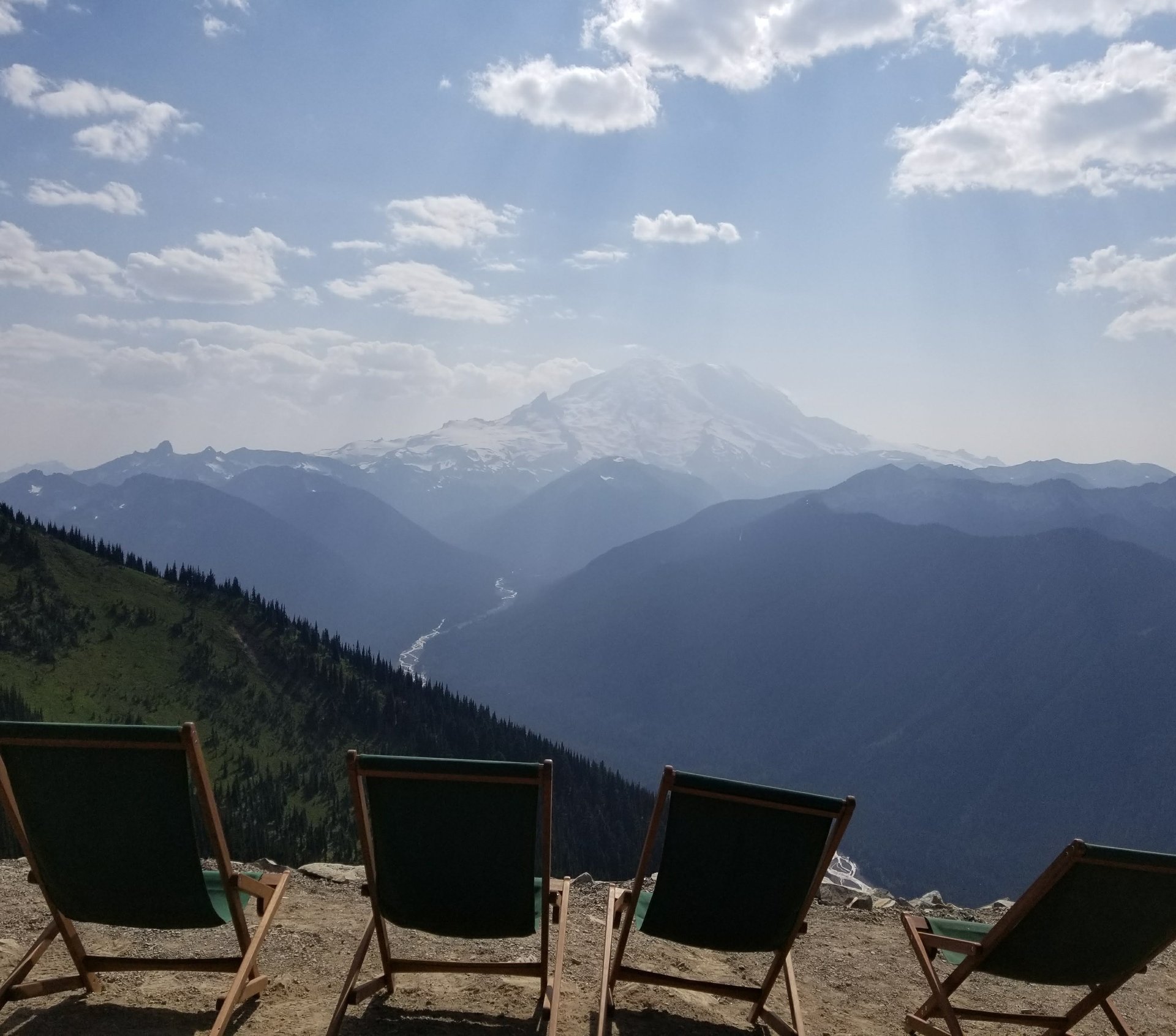 Green deck chairs facing Mount Rainier across a forested valley